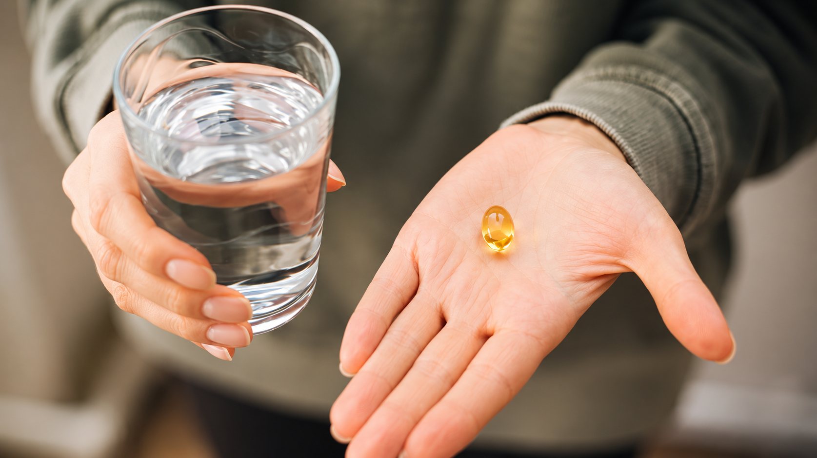 Une personne tient un verre d’eau dans une main et une capsule de gel jaune dans la paume de l’autre main.